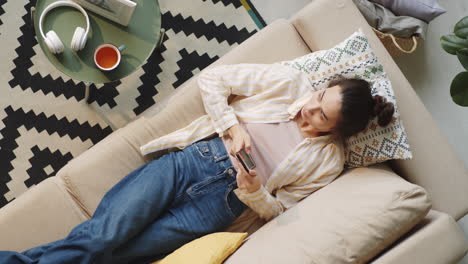 Mujer-Descansando-En-El-Sofá-Y-Usando-Un-Teléfono-Inteligente